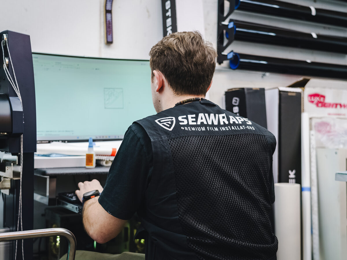 An installer at the PPF plotter inside SeaWraps, the founder's shop, with film rolls on the wall