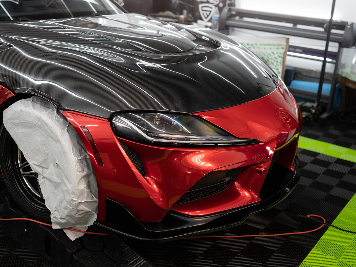 A red Toyota GR Supra mid PPF install at SeaWraps, masking paper over the wheel, plotter in the background